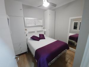 a white bedroom with a bed with purple sheets at Apartamento Solis in Chipiona