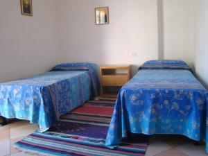 ムラヴェーラにあるAppartamento Deleddaの青いカバーとテーブル付きのベッド2台が備わる客室です。