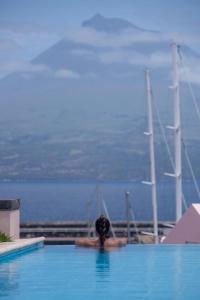 a person in a swimming pool with a boat in the water at Azoris Faial Garden – Resort Hotel in Horta
