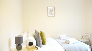 Heathrow Ensuite Rooms في ستانويل: سرير عليه شراشف بيضاء ومصباح