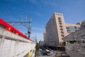 a red train traveling down a city street with buildings at Meitetsu Toyota Hotel in Toyota