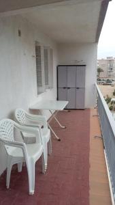 eine Terrasse mit weißen Stühlen und einem Tisch auf dem Balkon in der Unterkunft La Pineda III in La Pineda