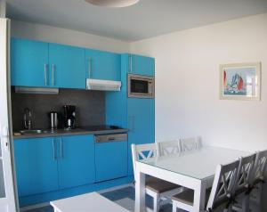 een keuken met blauwe kasten en een tafel en stoelen bij Résidence Odalys Le Domaine des Dunettes in Cabourg