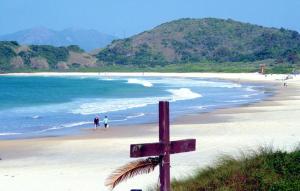a wooden cross on a beach with people in the water at Casa a 50 mt da Praia. in Bombinhas