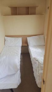 2 bedden in een kleine kamer met witte lakens bij 8 BERTH CARAVAN TP60 ON THE GOLDEN PALM CHAPEL ST LEONARD in Chapel Saint Leonards