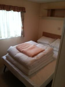 a bedroom with a bed with white sheets and a window at 8 BERTH CARAVAN TP60 ON THE GOLDEN PALM CHAPEL ST LEONARD in Chapel Saint Leonards