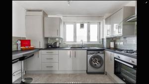 Lovely One Bedroom Apartment in Stratford في لندن: مطبخ بدولاب بيضاء وغسالة ملابس
