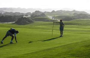 two people standing on a green golf course at Praia Del Rey ViewPool Sea in Amoreira