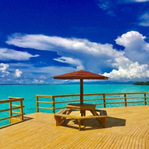 a wooden deck with an umbrella on the water at Amoa Resort Savaii in Tuasivi