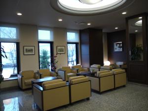 a waiting room with yellow chairs and tables and windows at Hotel Route-Inn Gifuhashima Ekimae in Hashima