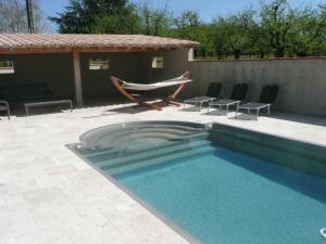a swimming pool with chairs and a hammock next to a house at Gîte de Beausoleil in La Romieu