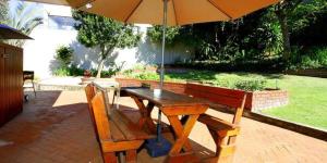 a wooden table and chairs with an umbrella at Die Strandhuis in Umdloti