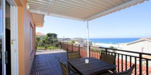 a balcony with a wooden table and chairs and the ocean at Die Strandhuis in Umdloti