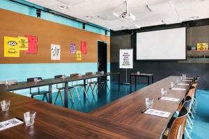 una sala de conferencias con mesas y una pantalla blanca en The Social Hub Amsterdam West, en Ámsterdam