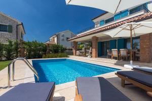 een zwembad met stoelen en een parasol naast een huis bij Luxury Villa Maša in Dobrinj