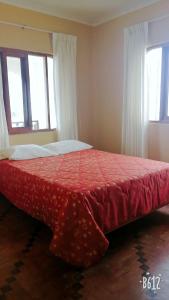 a bedroom with a red bed with two windows at Hospedaje Casablanca in Pisco