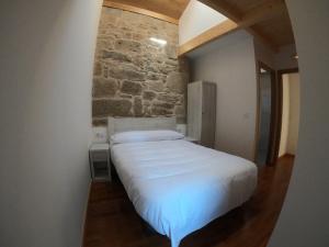 a bedroom with a white bed with a stone wall at Albergue A Salazon in Villanueva de Arosa