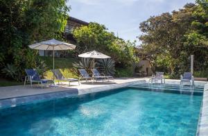 a swimming pool with chairs and umbrellas in front of a house at Pousada Vila Pitanga in Búzios