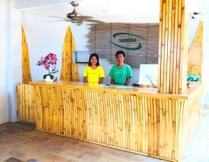 two people standing behind a wooden counter with surfboards at Samba Villas Beachfront View in Gili Trawangan