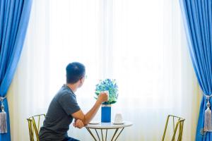 un homme assis à une table devant une fenêtre dans l'établissement VF Hotel Dalat, à Đà Lạt