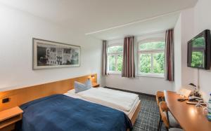 um quarto de hotel com uma cama, uma secretária e janelas em City Hotel em Eisenach