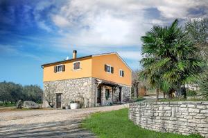 a yellow house with a palm tree and a stone wall at Rooms Agroturizam Romano in Buje
