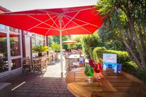 - une table en bois avec un parasol rouge sur la terrasse dans l'établissement Kyriad Nîmes Ouest A9, à Nîmes