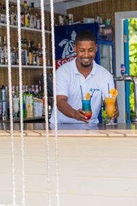 a man standing behind a counter with two cocktails at Le Nautique Waterfront Hotel La Digue in La Digue
