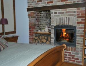 a bedroom with a brick fireplace with a bed at Chambres d'hôtes La Petite Flambée in Le Tronquay