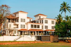 a large white building with palm trees in the background at Sol De Goa by Sereno in Candolim