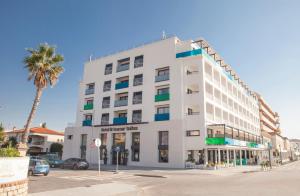 a white building with a palm tree in front of it at Hotel Brisamar Suites in Comarruga