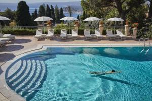 a man swimming in a pool with a blue umbrella at Grand Hotel Timeo, A Belmond Hotel, Taormina in Taormina