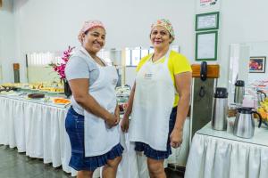 two women standing next to tables in a kitchen at Pousada Paraiso in Guanamby