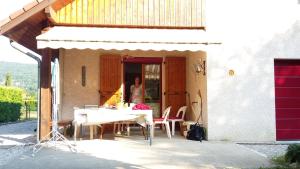 Eine Frau steht vor einem Haus mit einem Tisch und Stühlen. in der Unterkunft vue sur les montagnes dans maison au calme in Saint-Joseph-de-Rivière