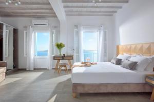 a white bedroom with a large bed and windows at Amelie Suites in Agios Stefanos