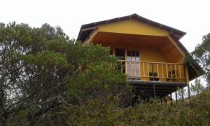 a yellow house on top of a hill with trees at Cabaña Los Llanitos Guatavita in Guatavita