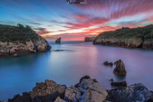 a sunset over the ocean with rocks in the water at Apartahotel Trébede in Barro de Llanes