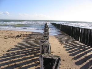 a row of wooden posts on a beach near a body of water at Vakantieoord "de Peppelhoeve" in Koudekerke