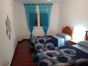 ビラガルシーア・デ・アロウサにあるPiso en Villagarcia de Arosaの青いカーテンと窓が備わる客室で、ベッド2台が備わります。