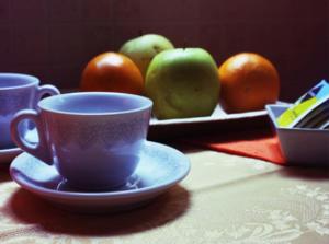 a table with a cup and a plate of apples and oranges at Affittacamere Pone in Sesto San Giovanni