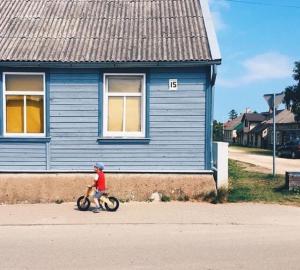 Un niño montando una bicicleta por una calle delante de una casa azul en Pie Jūras Pāvilostā en Pāvilosta
