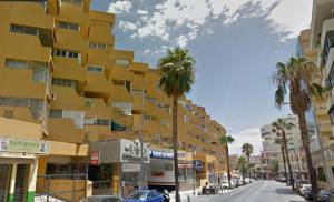 żółty budynek przy ulicy miejskiej z palmami w obiekcie Moderno apartamento Torremolinos centro w mieście Torremolinos