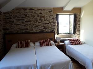 2 camas en una habitación con una pared de piedra en Pension Albergue Alborada, en Salceda