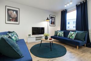 a living room with blue couches and a tv at Pušyno apartamentai in Anykščiai