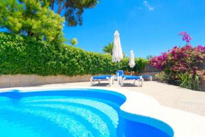 a swimming pool with two chairs and an umbrella at Beach Villa Carmen in Playa de Muro
