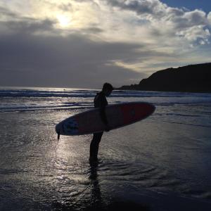 um homem parado na praia segurando uma prancha de surf em QUILLET COTTAGE, 2 GLENTOWAN ROAD em St Austell