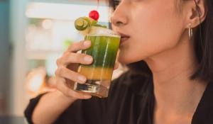a woman drinking a drink with a cherry on top at CROWN PRINCE Hotel Surabaya Managed by Midtown Indonesia in Surabaya