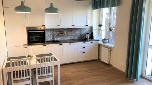 a kitchen with white cabinets and a table with chairs at Lux Garden Apartment in Kołobrzeg