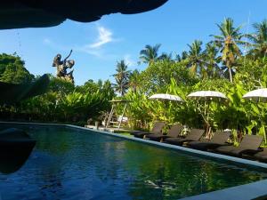 una piscina en un complejo con sillas y sombrillas en Gangga Blessta Hotel, en Ubud