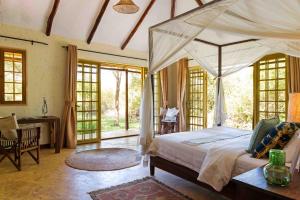 ein Schlafzimmer mit einem großen Himmelbett und einem Schreibtisch in der Unterkunft Kili Villa Kilimanjaro Luxury Retreat in Arusha